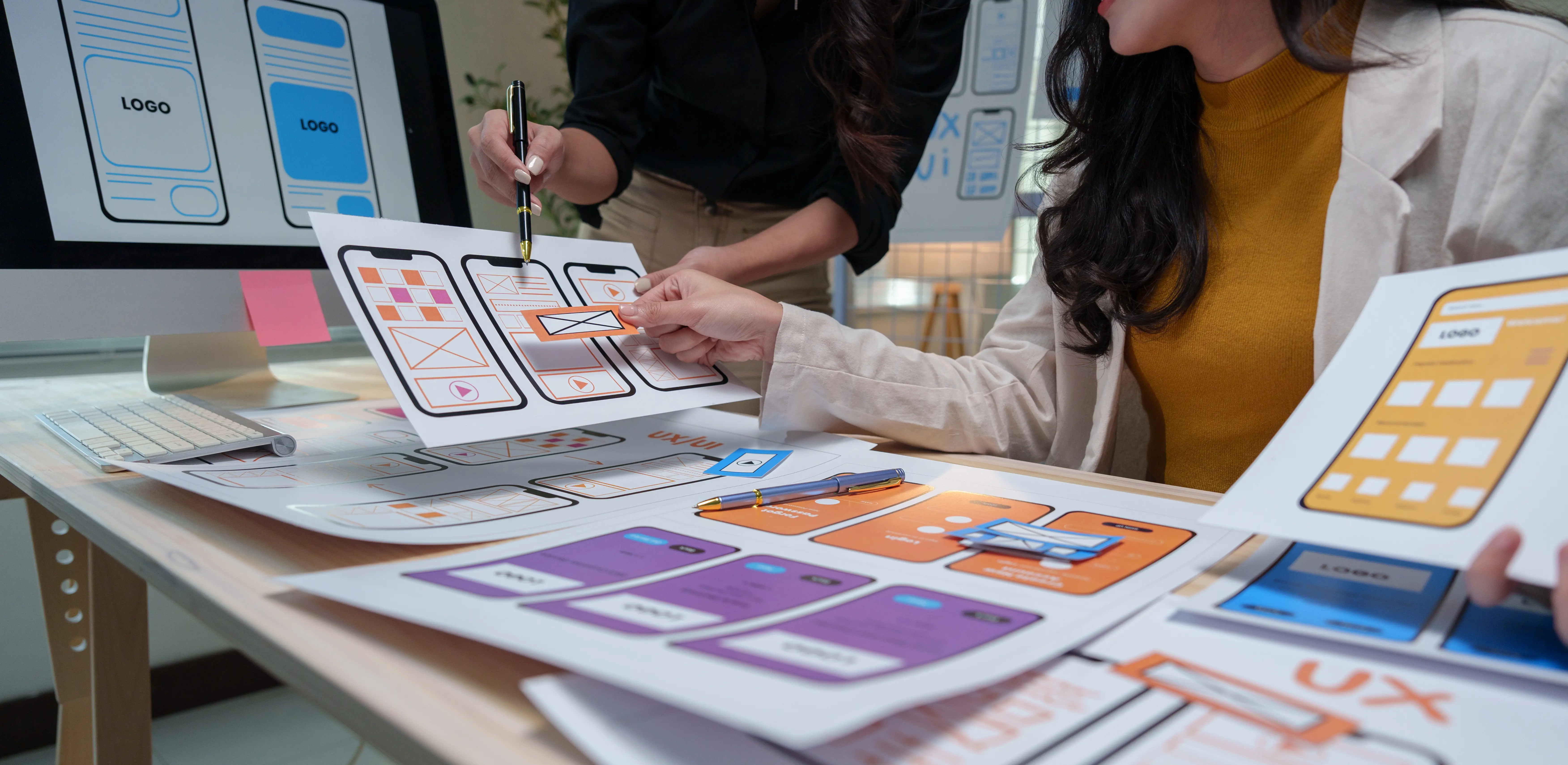 Design professionals reviewing mobile app wireframes and user interface layouts, collaborating on user experience improvements and application design concepts.